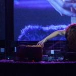 Merche Blasco performs at New York's La Mama Experimental Theatre Club, leaning over a soundboard and against several screens showing close-ups of her performance Photo Credit: Mariana Oriente