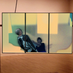 Image: A rectangular screen sits, suspended in air, on a custom-made metal frame within a gallery-like setting. The screen is separated into three parts, with a collage-like image placed within.