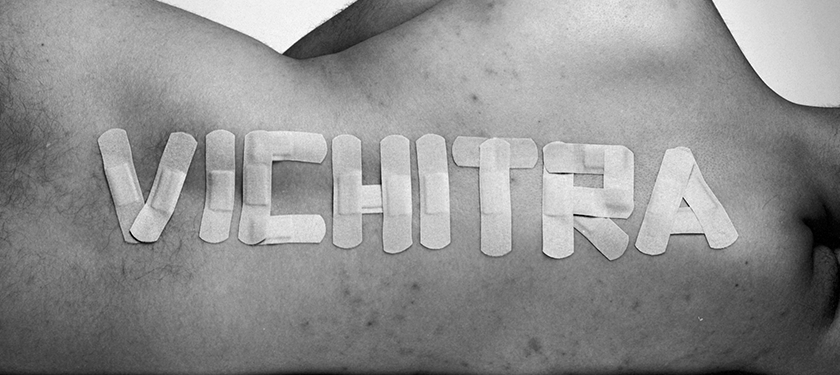 Black and white photo of a body laid down on its side, its back faces the viewer and the word "vichitra" is written on it with band-aids
