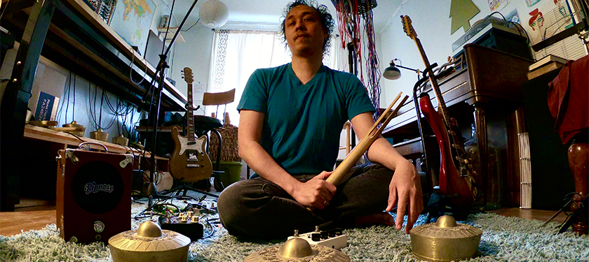 Chaitanya Tamayo poses in a room sitting on a carpet and surrounded by musical instruments