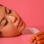 Image of an individual resting her head on a pink table with sausages