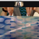 Image: An online studio visit being conducted by Zoom. Artist Ann Tarantino holds her work close to the screen for a detailed look as Heather Bhandari views the presentation.