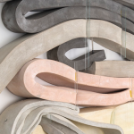 Twisted bars of cement, polyurethane, and foam in pastel colors over a white wall