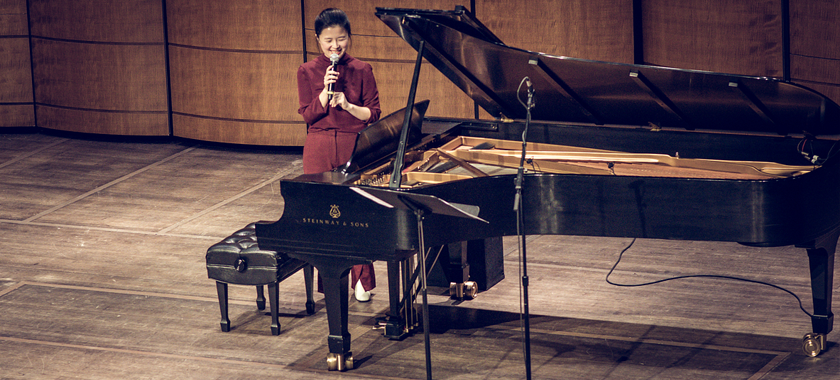 Image: Eunbi Kim stands on stage with a microphone in hand, addressing an unseen crowd at The Kennedy Center in Washington, DC.