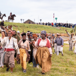 Image Detail: Dread Scott's "Slave Rebellion Reenactment," featuring contemporary people in historical garb, marching in Louisiana and armed with prop machetes, sickles, and muskets with flags flying.