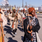 Image Detail: Dread Scott's "Slave Rebellion Reenactment," featuring contemporary people in historical garb, marching in Louisiana and armed with prop machetes, sickles, and muskets.