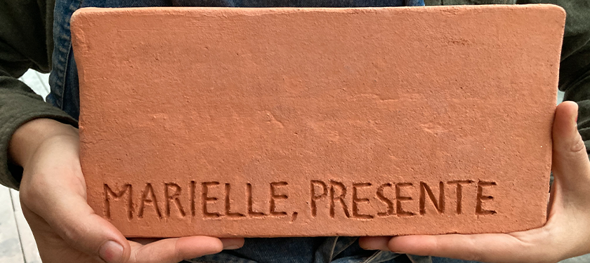 Two hands holding a brick that says "Marielle, presente"