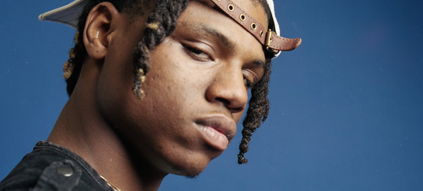 Image: Detail of a close-up portrait of Kane Wave, a hip hop artist from Buffalo, NY; Wave wears a backwards ball cap and is photographed giving the camera a side-long glance