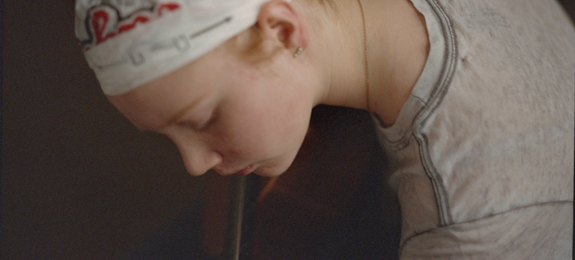 Image Detail: a color photograph of a young girl with a plastic bag on her head playing guitar in low light.