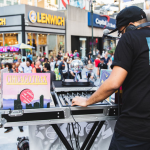 Image: A DJ wearing a black tee shirt, pants, and a hat performs at Plaza33 with turntables and electronic equipment; a record called "CHICAGOTRAX" is propped up with their setup.