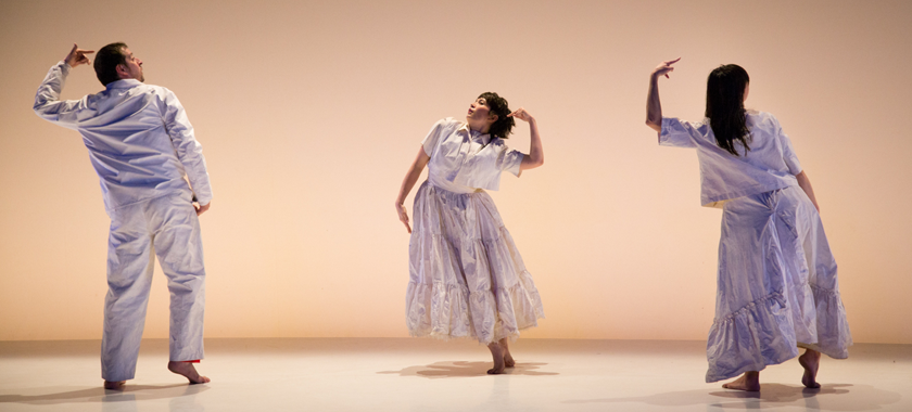 Image: Photo by John Cyr for "State of Heads." Three performers in white against a white backdrop and floor, evenly spaced apart. Left figure, Levi Gonzales is facing back, leaning to the left with left finger pointing to head, center figure, Rebecca Serrell Cyr, is facing front, leaning to the leaning to the left with left finger pointing to head, figure on the right, Hristoula Harakas is facing back, leaning to the left with left finger pointing to head.