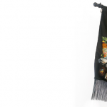 Image: photo of a black flag with fringe and elaborate embroidery featuring a mini van, Pine Sol, an international calling card, a doll's house, and other cultural references from the artist's childhood.