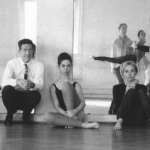 Image: Detail of a black and white photograph by Robert Rauschenberg of five individuals (including Rauschenberg) seated against a dance studio mirror, four dancers reflected back at us, the viewer.