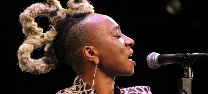 Image: Detail of a photograph of Nigerian-British musician Wunmi, pictured from her shoulders up in profile singing into a microphone.