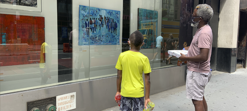 Image: Two individuals stand on a city sidewalk, looking into glass store windows at an Art on the Avenue display of colorful artworks.