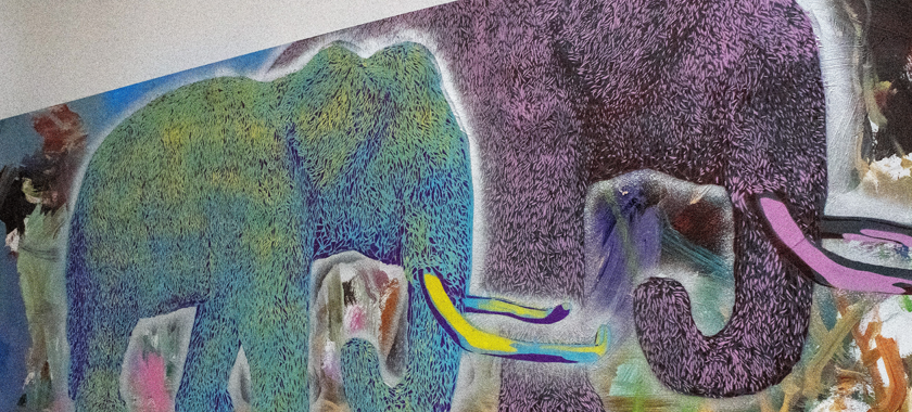 Image: Close-up of a painting by Ernesto Ibanez; a full-sized purple elephant is pictured next to a smaller elephant who is depicted in yellow, blue, and green