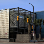 Image: Exterior of Centro De Artes Gallery, one part of the building is blue painted concrete and another a more transparent gridded section of cut metal panels with delicate designs.