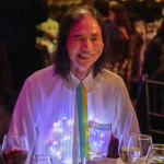 Artist Chin Chih hang, seated at dinner and smiling with a heart-shaped light display under his button down shirt