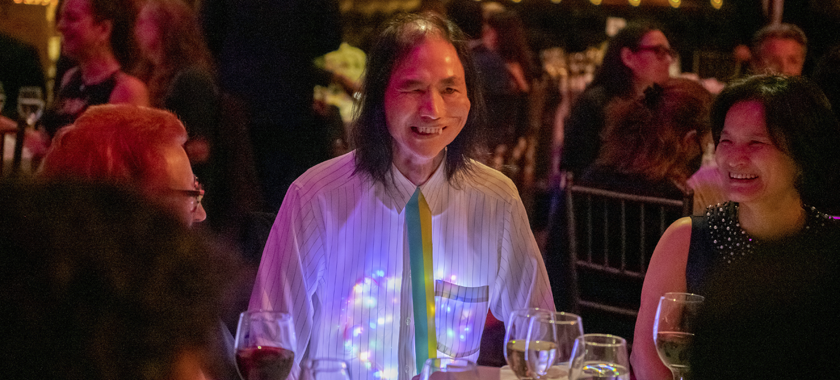 Artist Chin Chih hang, seated at dinner and smiling with a heart-shaped light display under his button down shirt