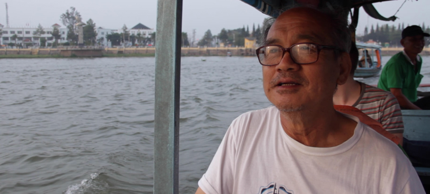 Photograph of a man in glasses and a white tee shirt on a boat on the water.