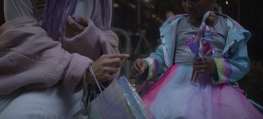 A little girl holding a doll reaches out to receive a sequin from the person sitting next to her.