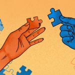 Blue and orange puzzle pieces have been joined together in the light orange background. In the foreground, a dark orange hand holding a dark orange puzzle piece is about to join it to a blue piece that is held by a blue hand on the right.