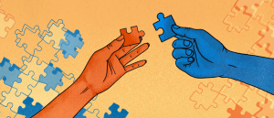 Blue and orange puzzle pieces have been joined together in the light orange background. In the foreground, a dark orange hand holding a dark orange puzzle piece is about to join it to a blue piece that is held by a blue hand on the right.