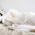 "Passage" was an immersive audio and video installation that encompassed 1500 sq. ft. of the ISE Foundation (New York) composed of 4-video projections, a surround sound audio, and 3-tons of white marble chips. Vangeline is lying on a bed of marble chips. She is wearing a long romantic white gown and her body is painted white, with red lipstick.