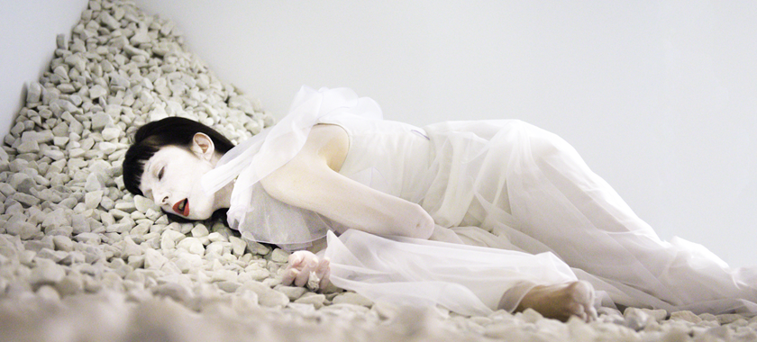 "Passage" was an immersive audio and video installation that encompassed 1500 sq. ft. of the ISE Foundation (New York) composed of 4-video projections, a surround sound audio, and 3-tons of white marble chips. Vangeline is lying on a bed of marble chips. She is wearing a long romantic white gown and her body is painted white, with red lipstick.