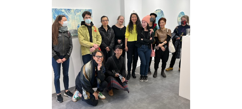 Image: Group shot of IAP artists posing together and smiling in a gallery space, with art on the walls behind them