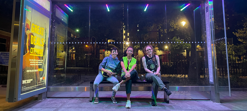 The film's ("Sequin") AD, Director, and DP sit in a sidewalk bus shelter that is illuminated with rainbow lights.