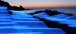 Ribbons of electric blue light cascade over the coastline as the sun sets.