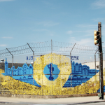 Large-scale blue and yellow art installation woven into a chain-link fence in Staten Island.