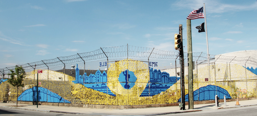 Large-scale blue and yellow art installation woven into a chain-link fence in Staten Island.