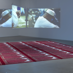 Floating 4-channel installation in a gallery space with red prayer mats below on the ground.