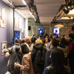 A crowded gallery space with paintings, drawings, and digital art on screens