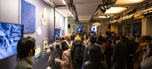 A crowded gallery space with paintings, drawings, and digital art on screens