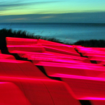 Ribbons of electric magenta light cascade over the coastline as the sun sets.