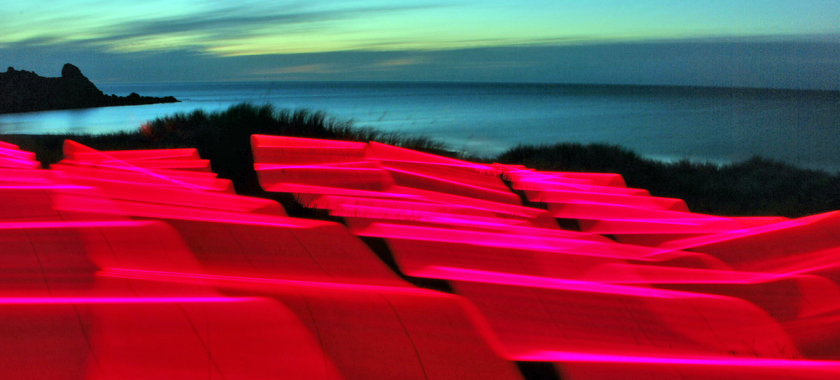 Ribbons of electric magenta light cascade over the coastline as the sun sets.