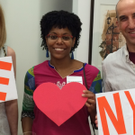 Three individuals with "We (Heart) NYFA" signs
