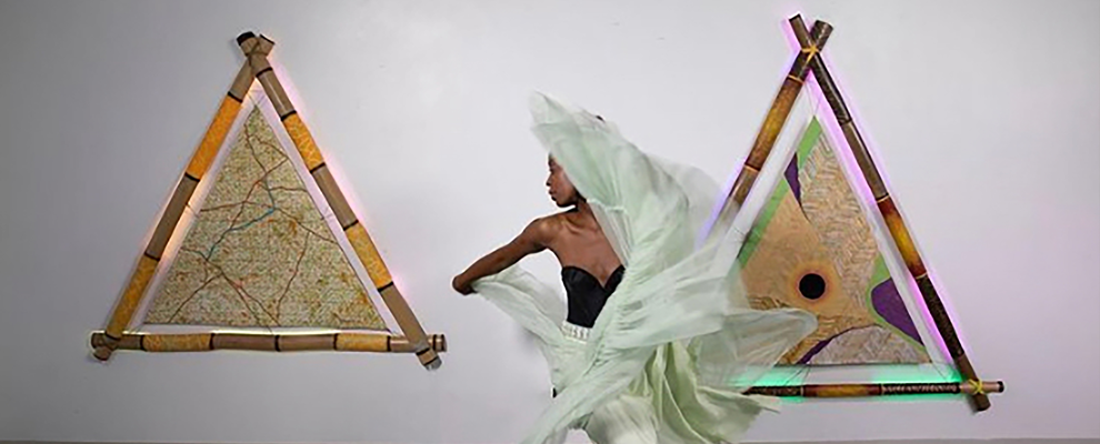 A dancer performs in a gallery. Behind them are pyramid shapes made from bamboo and neon lights.