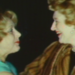 Video still of two women with blonde hair arms out going into an embrace
