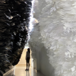Detail of an art installation by Jennifer Wen Ma. An individual stands in a canyon of paper feathers--black on the left and white on the right