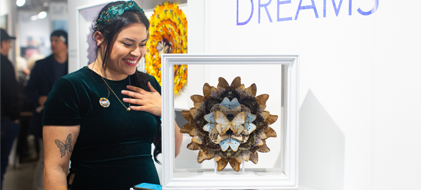 An individual with a butterfly tattoo on their arm smiles down at an artwork featuring images butterflies