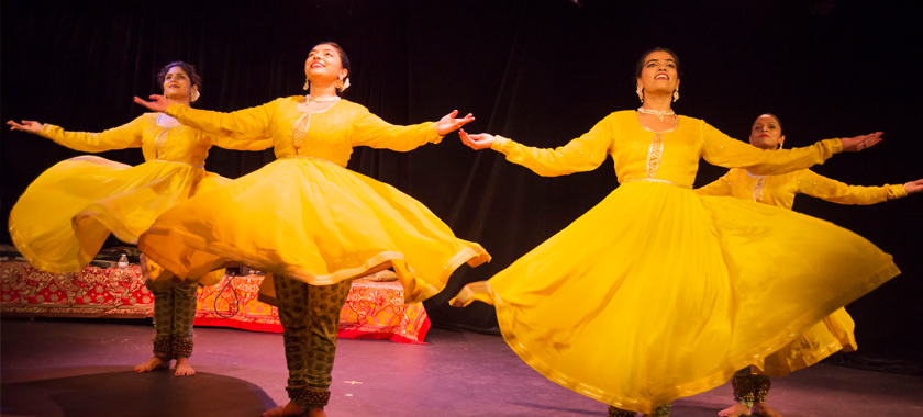 Four kathak dancers in yellow dresses arrive at "sam" or the finishing pose in kathak.