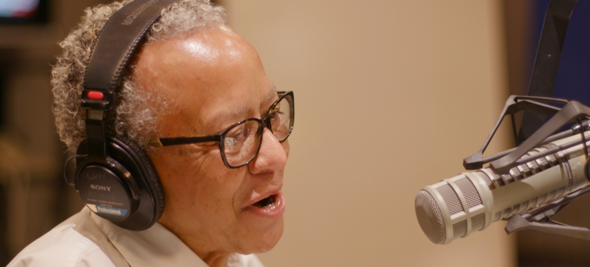 Image of Nikki Giovanni wearing headphones and speaking into a microphone