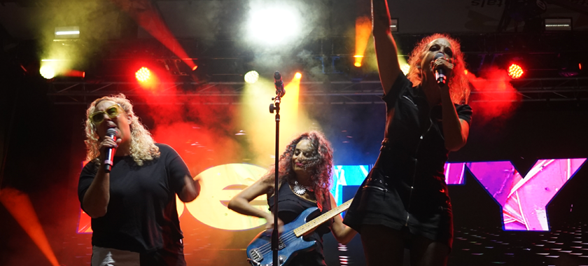 The three women of BETTY rocking out on big stage with very dramatic lighting