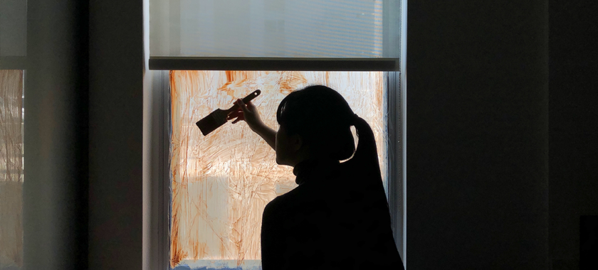 A person holding a brush painting on the window with acrylic, making the window dirty and blurry.