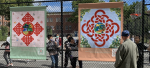 Two vinyl banner artworks are hung on a city park fence. Each has a red string element surrounding a circular center graphic. QR codes encourage interactivity.