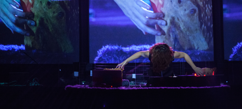 Merche Blasco playing an instrument made out of water, wood, electronics, and custom software, with screens behind them.